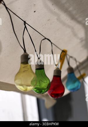 Bunte Lichterketten mit roten, gelben, grünen und blauen Glühbirnen am Kabel, aus einem niedrigen Winkel mit weichem Bokeh-Hintergrund im Outdoor-Set aufgenommen Stockfoto