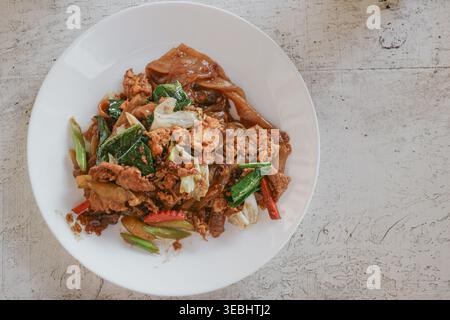 Sehen Sie, wie Thai-gebratene Nudeln mit Schweinefleisch auf einem rustikalen Tisch mit echter Street Food-Szene dargestellt werden. Stockfoto
