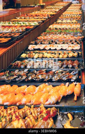 Dokumentarfilm Weitwinkel einer Sushi-Ausstellung auf einem geschäftigen thailändischen Markt. Die authentische Fusionskultur und das Catering lokaler Kleinunternehmen. Stockfoto