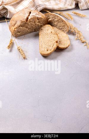 Deftiges Vollkornbrot, frisch gebacken und in Scheiben geschnitten, auf einer hellen Oberfläche mit Weizenohren und einem karierten Tuch, was auf gesunde Ernährung und Tradition hindeutet Stockfoto