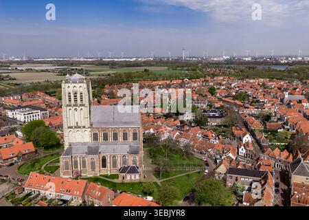 Seitenansicht des gotischen Kirchturms von Brielle mit Windturbinen und Hafenindustrie am Horizont Niederlande Stockfoto