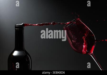 Rotwein von satter Farbe, der aus einer Flasche in ein Glas gegossen wird. Kopierbereich. Stockfoto