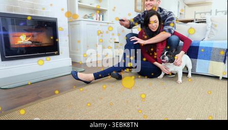 Kuschelndes Paar auf Teppich am Kamin, Mann mit Fernbedienung, Frau mit rotem Top-Wiegenhund Stockfoto