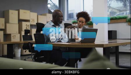 Zeigender Mann mit hellblauem Hemd, Frau mit grauem Blazer, die sich im Büro über den Laptop beugt Stockfoto