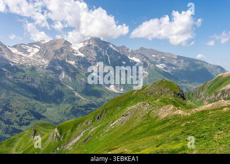Alpenberg Panorama Landschaft grüne Grate felsige Hänge entfernte schneebedeckte Gipfel blaue Himmel Wolken. Weite Hügellandschaft. Dramatische Landschaft Stockfoto