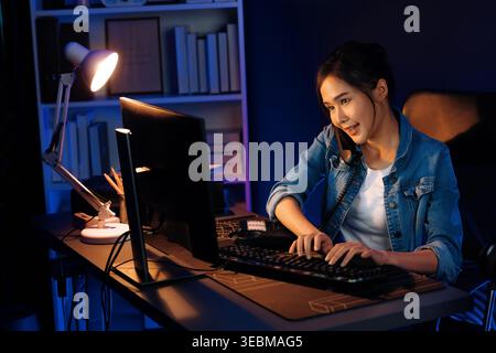 Junge schöne asiatische kreative Frau, die am Telefon mit Kunden oder Kollegen anruft und den hohen Gewinn des Schöpferprojekts erklärt, während sie auf der Suche nach dem Markt ist Stockfoto