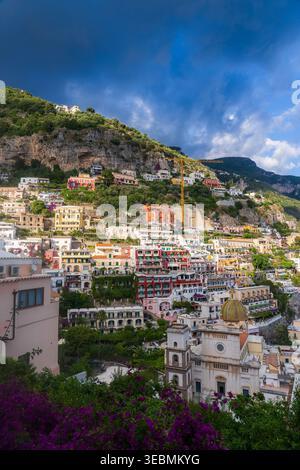 Blick auf farbenfrohe Gebäude, die unter einem dramatischen Himmel den Hügel hinunter fallen, bietet einen Einblick in den lebhaften Charme von Positano, Kampanien, Italien. Stockfoto