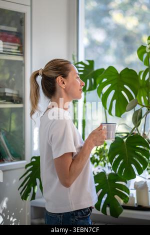 Lächelnde positive, reife Frau genießt friedliche Morgenzeit und aromatischen Kaffee zu Hause am Wochenende. Stockfoto