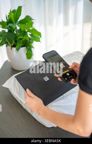Smartphone scannt kleinen QR-Code auf dem Paket mit Fokus auf dem Etikett für die Nachverfolgung der Zustellung zu Hause. Kontaktlose Identifizierungs- und Logistiktechnologie Stockfoto