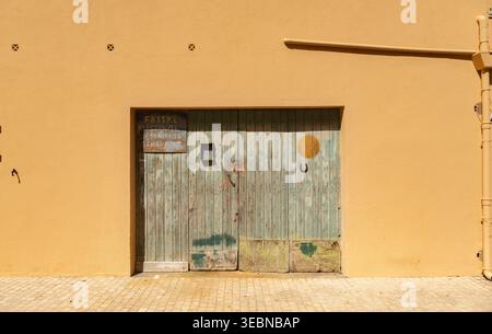 Verwittertes Hölzernes Garagentor Mit Pastelltürkis In Gelber Stuckfassade Mit Sonnensymbol Stockfoto