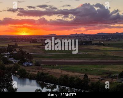 Aus der Vogelperspektive auf den farbenfrohen Sonnenuntergang über dem Morpeth River und dem umliegenden Ackerland in New South Wales, Australien. Malerische ländliche Landschaft mit lebendigem Himmel Stockfoto