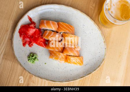 Lachs-Sushi-Rolls Mit Bier. Blick von oben auf Lachs-Sushi-Brötchen mit eingelegtem Ingwer, Wasabi und Bier auf einem hölzernen Restauranttisch. Stockfoto