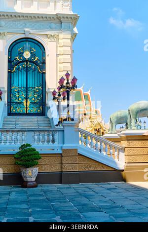 BANGKOK, THAILAND - 28. Februar 2025: Goldene Türme des Grand Palace Bangkok und weiße Wände mit Touristen auf gepflegtem Rasen unter blauem Himmel. Hochwertiges Foto Stockfoto