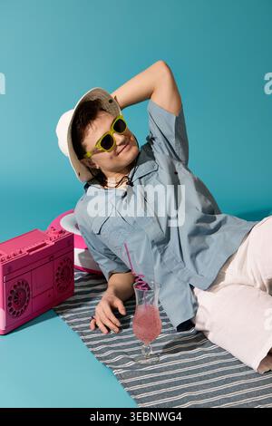 Charmanter junger Mann entspannt sich in Sommerkleidung, schlürft ein farbenfrohes Getränk und genießt fröhliche Momente. Stockfoto