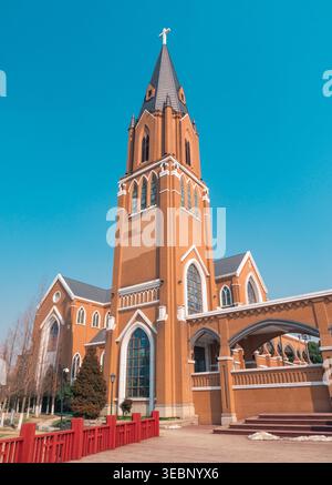 Kirchengebäude im gotischen Stil mit einem hohen Turm und Kreuz, das tagsüber vor einem strahlend blauen Himmel steht Stockfoto