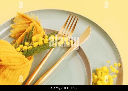 Nahaufnahme des Frühlingstisches mit Mimosa-Blüten und goldenem Besteck Stockfoto
