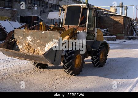 Frontlader bewegt im Winter Material in einem Industriewerk auf schneebedecktem Boden Stockfoto