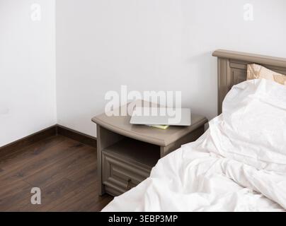 Laptop liegt auf einem Nachttisch im Schlafzimmer und unterstreicht die Integration moderner Technologien in entspannte Wohnumgebungen Stockfoto