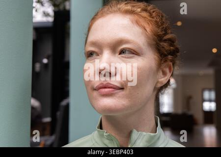 Frau mit hellgrünem Reißverschluss oben, die etwas direkt neben die türkisfarbene Säule und das Sofa blickt Stockfoto
