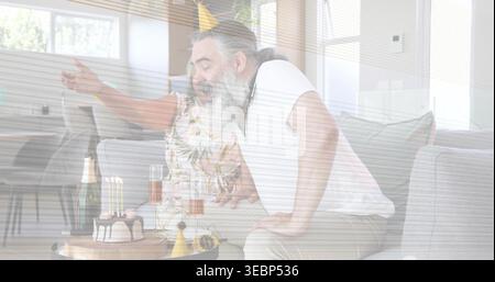 Lehnender Mann im T-Shirt, der Kuchenkerzen bläst, Frau in floraler Spitze, die auf dem Sofa Gesten macht, mit Champagner Stockfoto