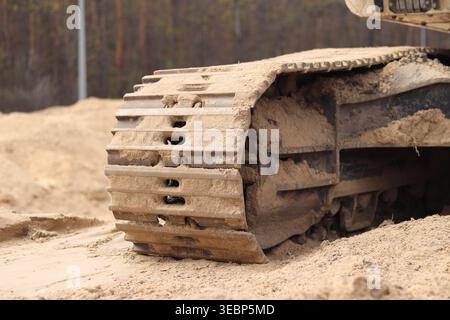 Baggerketten auf Sand aus nächster Nähe. Detaillierte Ansicht der leistungsstarken Metallspuren von Baumaschinen, die beim Arbeiten auf sandigem Boden mit Schlamm bedeckt sind Stockfoto