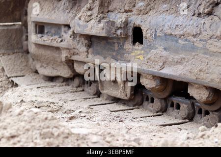 Baggerketten auf Sand aus nächster Nähe. Detaillierte Ansicht der leistungsstarken Metallspuren von Baumaschinen, die beim Arbeiten auf sandigem Boden mit Schlamm bedeckt sind Stockfoto