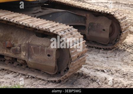 Baggerketten auf Sand aus nächster Nähe. Detaillierte Ansicht der leistungsstarken Metallspuren von Baumaschinen, die beim Arbeiten auf sandigem Boden mit Schlamm bedeckt sind Stockfoto