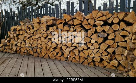 Holzscheite auf einem Stapel in der Nähe des Zauns. Brennholz einsatzbereit. Gestapelte Holzstämme. Nahaufnahme von gestapeltem Brennholz. Natürlicher Holzhintergrund Stockfoto