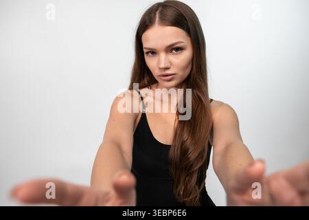 Junge Frau, die mit den Armen nach vorne streckt, direkt in die Kamera blickt, Konzept der Verbindung oder Einbeziehung Stockfoto