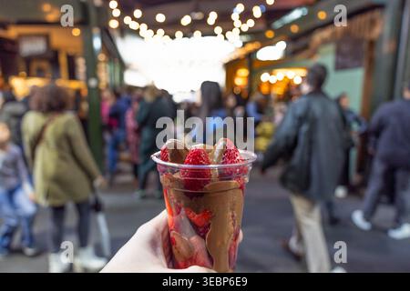 Hand in der Hand mit Schokolade überzogenen Erdbeeren auf einem geschäftigen Straßenmarkt Stockfoto