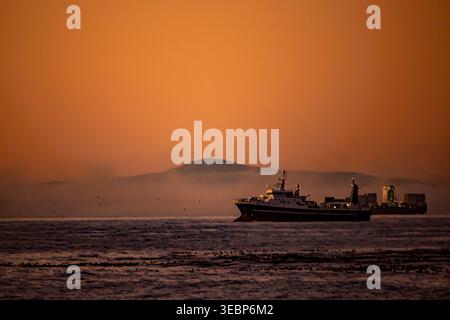 Große Schiffe in der Abenddämmerung, in Table Bay, Kapstadt, Südafrika, mit nur dem Gipfel eines Berges, der aus den Wolken entlang der Küste ragt Stockfoto