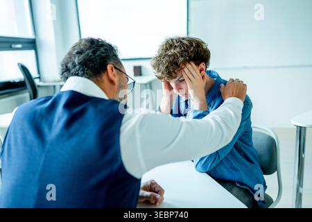 Lehrer, der sich um einen schwer wiegenden Schüler kümmert. Junge, der sich einem Lehrer anvertraut. Stockfoto