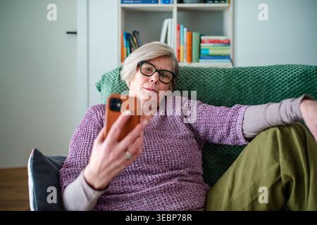 Eine ältere Frau liegt auf dem Sofa und blättert am Telefon. Stockfoto
