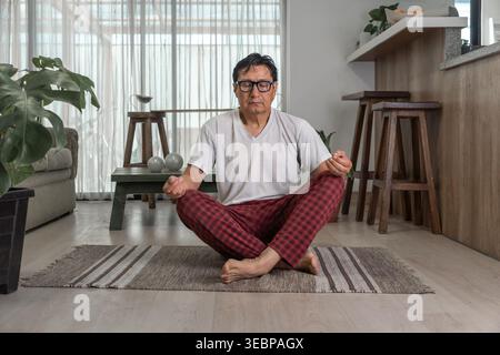 Senior Mann meditiert in einer Yoga-Pose auf einem Teppich in einer modernen Wohnung Stockfoto