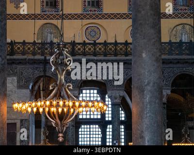 Prunkvoller, kreisförmiger goldener Kronleuchter mit leuchtenden Glühbirnen, die im majestätischen historischen Inneren der Hagia Sophia Moschee in Istanbul hängen Stockfoto