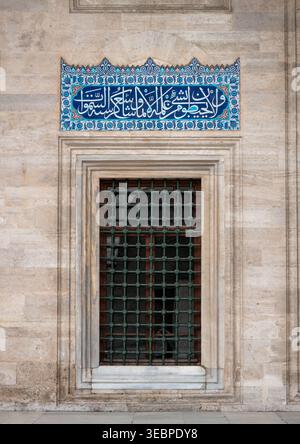 Komplexe arabische Kalligraphie auf blauen Iznik-Fliesen über einem traditionellen Gitterfenster in der historischen Steinfassade des Topkapi-Palastes Stockfoto