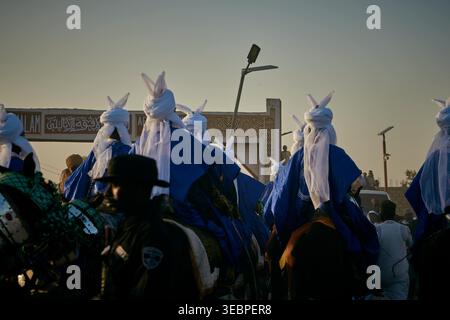 Zaria Stadt, Nigeria - 22. März 2026: Blick auf eine lebhafte Prozession von Reitern in markanter blau-weißer Kleidung, die sich unter einem weichen, goldenen Himmel bewegt. Stockfoto