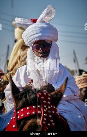 Zaria, Nigerian - 22. März 2026: Blick auf eine königliche Figur in strahlend weißer Kleidung und dunklen Tönen, auf einem dunklen Pferd mit markantem Rot-Nieten-T montiert Stockfoto