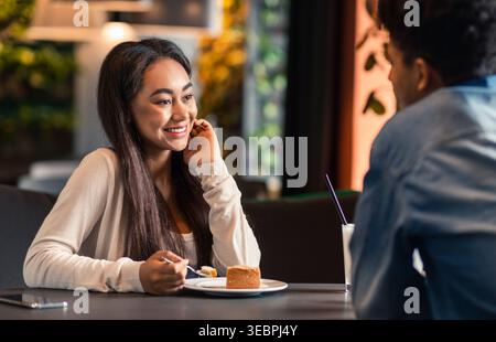 Frau genießt Dessert, während sie in einem Gespräch in einem modernen Café teilnimmt Stockfoto