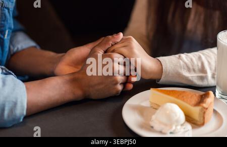 Zwei Personen halten Hände, während sie ein Dessert und einen Drink in einem gemütlichen Café genießen Stockfoto
