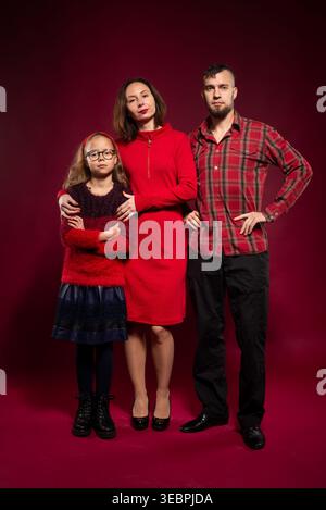 Eine dreiköpfige Familie in Red stellt sich zusammen auf dunkelrotem Hintergrund in Studio aus Stockfoto