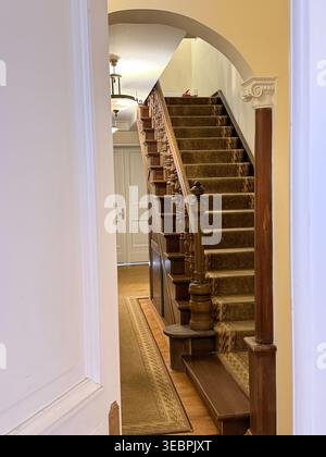 Holztreppe mit Teppich in klassischer Inneneinrichtung, Blick durch offene Tür von oben. Mobiles Foto Stockfoto