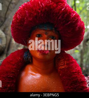 Munshiganj, Bangladesch - 13. April 2025: Blick auf eine Person mit markanter roter Federkleidung und Karosseriefarbe, deren Gesicht mit blauer Farbe versehen ist, gegen einen so Stockfoto