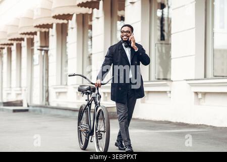 Mann, der tagsüber mit dem Fahrrad läuft und telefoniert, in urbaner Umgebung Stockfoto