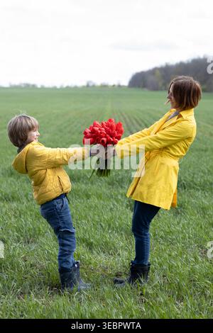 Preteen Son gratuliert seiner Mutter mit einem Strauß roter Tulpen. Alles Gute zum Muttertag. Blumen für gute Laune. Spaß mit Mom draußen haben. Helles y Stockfoto