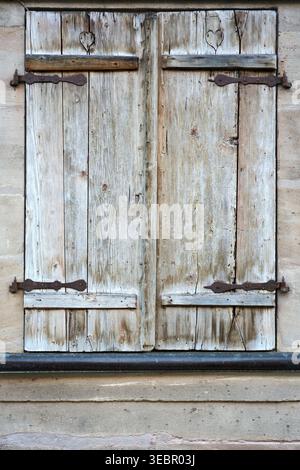 Nahaufnahme von verwitterten Holzfensterläden mit antiken rostigen Eisenscharnieren an einer Steinmauer. Rustikaler architektonischer Hintergrund für Vintage-Design. Stockfoto