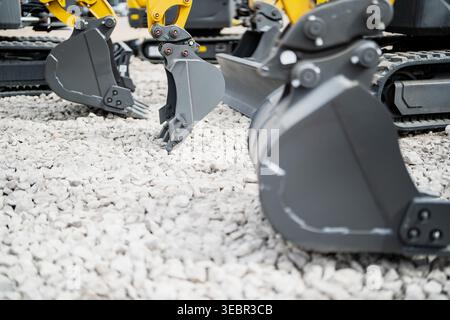 Mehrere Anbaugeräte für Minibagger mit gelben Auslegerarmen und Gummiketten auf Kies für die Anzeige von Mietflotten und den Einsatz im Baugewerbe Stockfoto