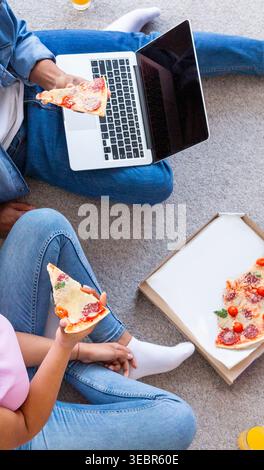 Genießen Sie Pizza und arbeiten Sie am Laptop, während Sie sich zu Hause entspannen Stockfoto