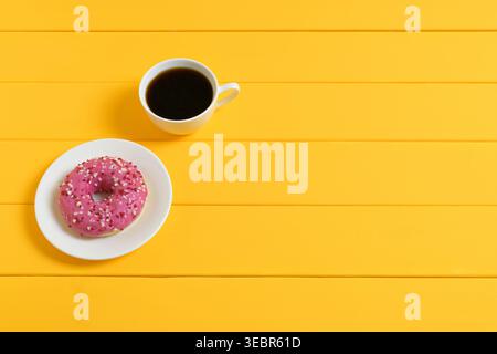 Kaffeetasse und rosa glasierter Donut auf gelbem hölzernem Hintergrund Stockfoto