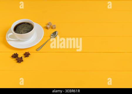 Kaffeetasse mit braunen Zuckerwürfeln, Löffel und Sternanis auf gelbem Hintergrund Stockfoto